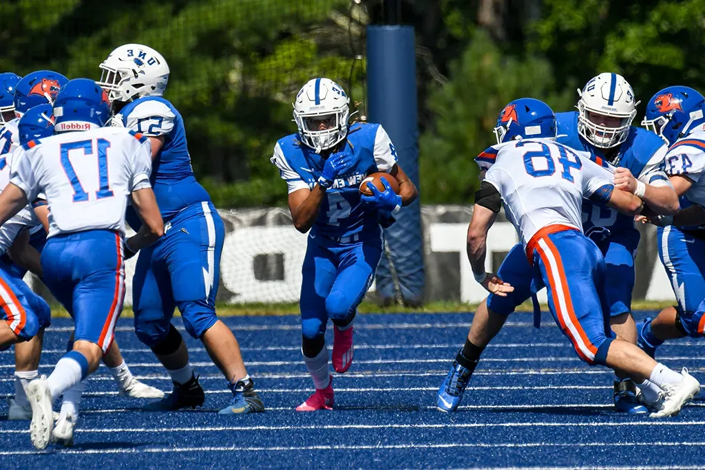 U N E football players during a game on the blue field