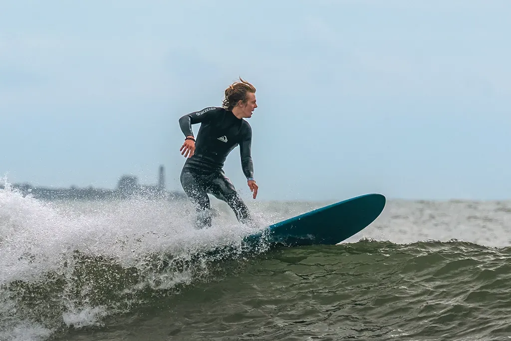 A student in a wetsuit catching a wave on a surfboard