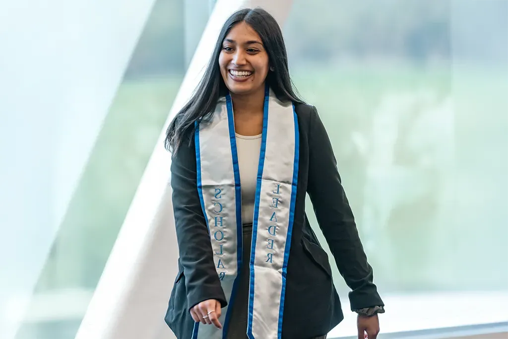 A U N E student wearing a sash that says "Leader" on one end and "Scholar" on the other