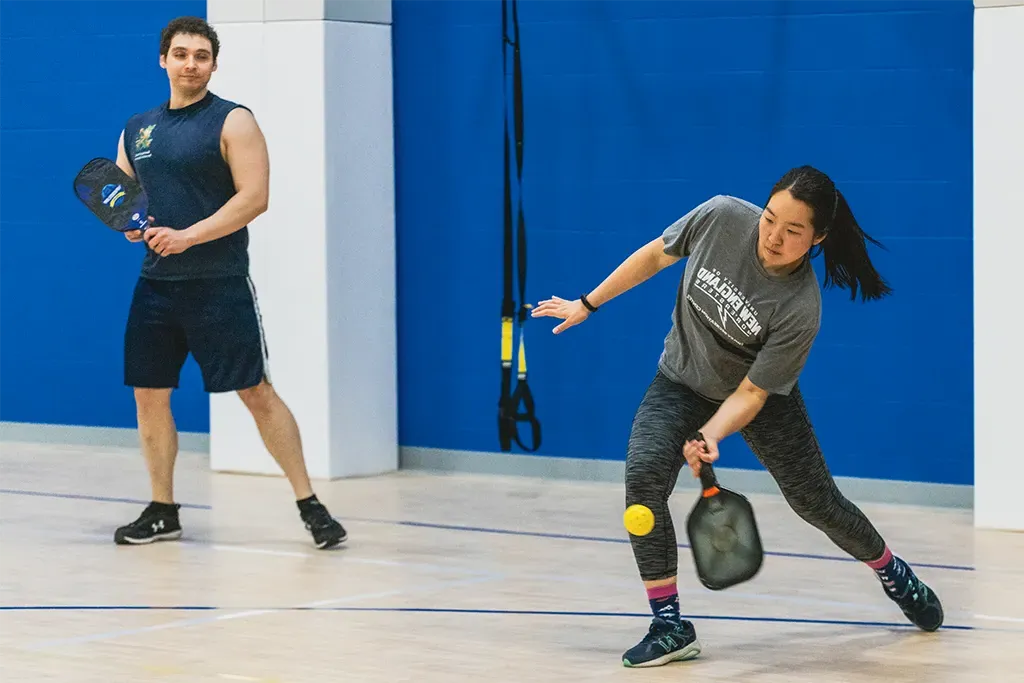 Two students play pickleball in a U N E gym